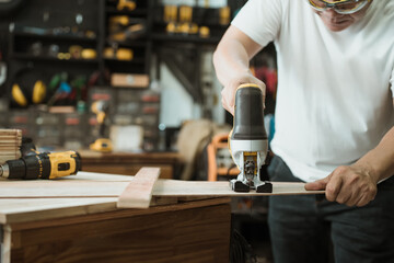 Carpenter cutting wooden with electric jigsaw in workshop, woodworking concept , selective focus