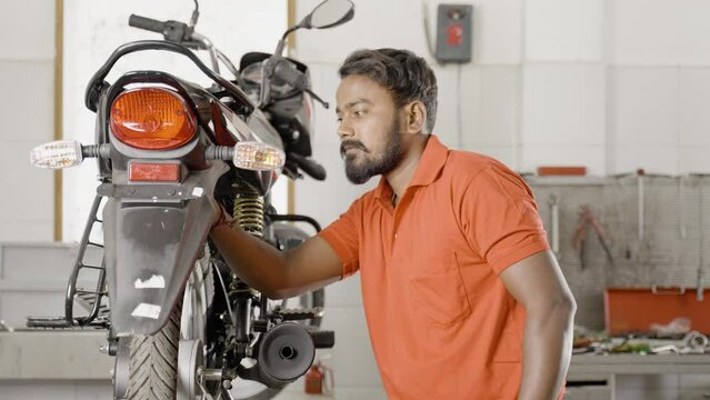 motorbike mechanic standing with crossed arms by looking at camera while reparing at garage - concept of repair or maintenance service and blue collar jobs