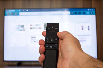 A hand holding a tv controller and a 50'' television in the background.