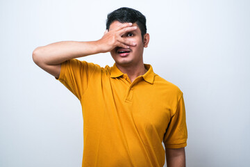 Obraz premium Young handsome man peeking in shock covering face and eyes with hand, looking through fingers with embarrassed expression.
