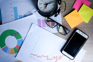 Messy office desk with paperwork, eyeglasses, smart phone and alarm clock 