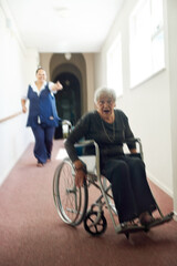 Fototapeta na wymiar Im busting out of this joint. Shot of a mischievous senior woman using her wheelchair to run away form her nurse in an old age home.