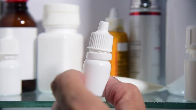 hand picking eye drops bottle from medicine cabinet