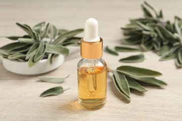 Bottle of essential sage oil, plant twigs and leaves on wooden table.