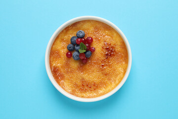 Delicious creme brulee with fresh berries and mint on light blue background, top view