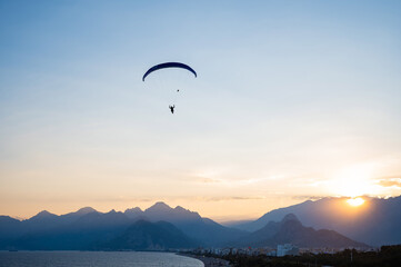 Silhouette of a man on a paraglider flying over the sea at sunset.