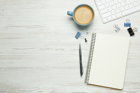 Blank notebook, cup of coffee, computer keyboard and office stationery on white wooden table, flat lay. Space for text