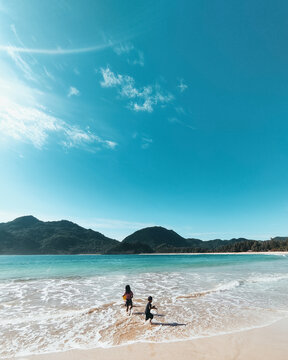 Beautiful Landscape View Of Two Kids Playing In Water Beach With Mountains With A Sunny Blue Sky