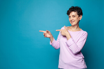 Mid adult woman smiling and  pointing finger on blue studio background