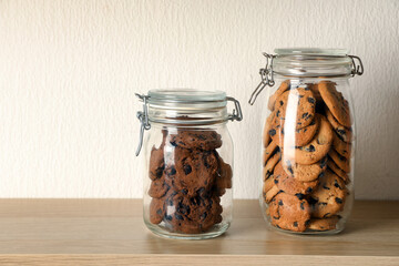 Delicious chocolate chip cookies in glass jars on wooden table