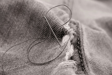 Hole in jeans. Needle with thread for darning jeans. Tools for work dressmaker, seamstress fashion designer - obrazy, fototapety, plakaty