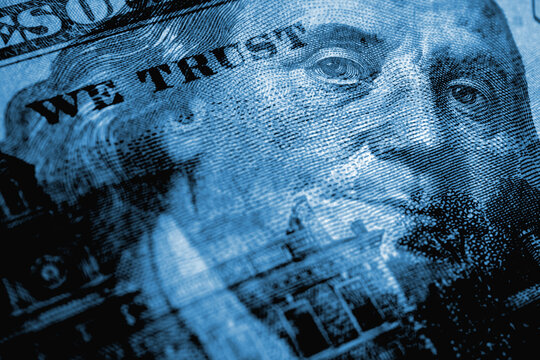 American paper money. A 100 dollar bill with a portrait of Benjamin Franklin in focus. US banknotes closeup. Dark blue tinted background about Public debt. Reserve or anchor currency. Macro