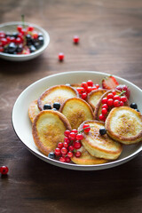 pancakes with berries, black and red currants in a white plate on a brown wooden background vertical photo