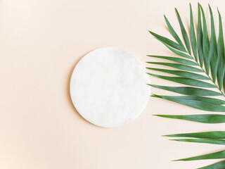 Marble white round podium and green palm leaf on beige background.
