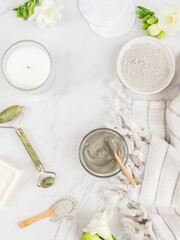 Organic blue clay for beauty facial mask., crystal massager, candle, cotton towel and white flowers on marble background.