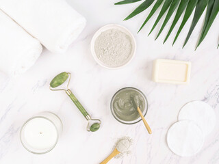 . Organic blue clay for beauty facial mask, crystal massager, cotton pad, soap, candle, cotton towel and palm leaf on marble background