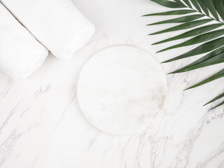 Marble white round podium, cotton towelsand green palm leaf on marble background.