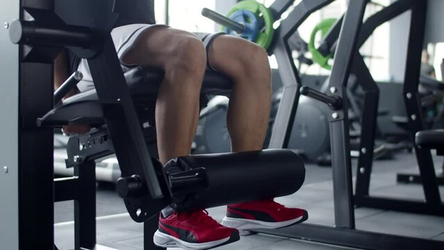 Man trains in gym on an exercise machine for legs lifting heavy weight, side view. Man trains legs on training machine in gym. Concept workout