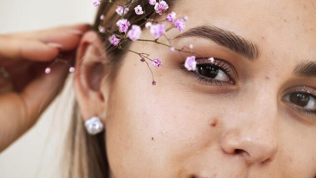 Girl's face with clean smooth skin, naked makeup on the background of gypsophila branches in the studio. Model