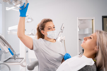 Woman dentist in the detal office preparing for treatment turns on the light and prepares the equipment. copy space.