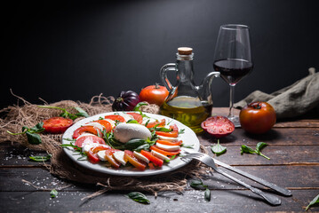 Typical Italian dish of cow or buffalo mozzarella cheese, with arugula, basil, tomato, olive oil, and coarse salt, typical of Caserta and Saleno, Italy and a glass of red wine.