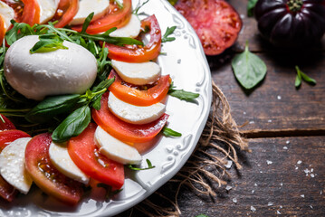 Typical Italian dish of cow or buffalo mozzarella cheese, with arugula, basil, tomato, olive oil, and coarse salt, typical of Caserta and Saleno, Italy.
