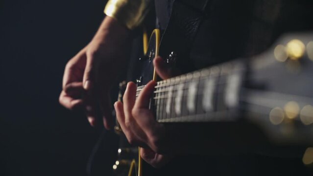 Male hands playing black electric guitar with golden mechanics filmed down the fretboard