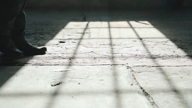 Male feet in cowboy boots walking in slow motion on concrete floor with window shadow falling on the ground
