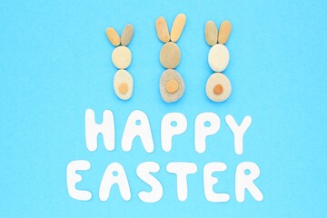 Happy Easter lettering and bunnies from pebbles on blue background. Flatlay postcard creative concept. 
