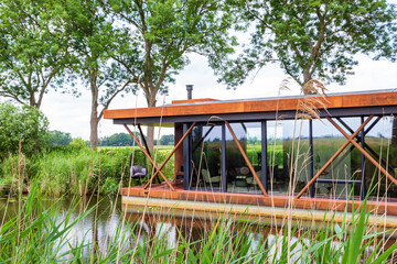 Fototapeta na wymiar New modern house boat industrial style in canal between reed and trees in The Netherlands