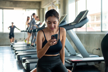 Asian athletic woman using mobile phone for social media or online shopping while workout exercise at fitness gym. Healthy female do sport training at sport club. Health care motivation concept