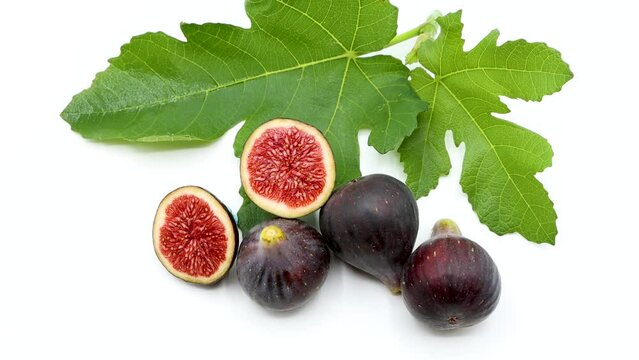 Delicious freshly picked ripe figs next to a green fig leaf on isolated white background