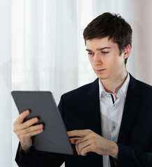close up caucasian businessman serious working with tablet, wear suit, standing, looking at tablet. Young man work business with home office background and copy space