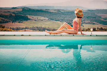 woman sitting by the pool with a cocktail  admiring green ladscape in Tuscany, Italy