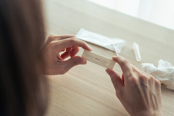 Self test of Coronavirus infected patient using ATK rapid test kit to check the positive result at home. Close up shot of woman holding antigen test kit with stress feeling to know the 2 stripe result