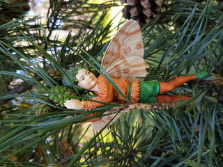 Closeup of a miniature gardening fairy statue on a fir branch