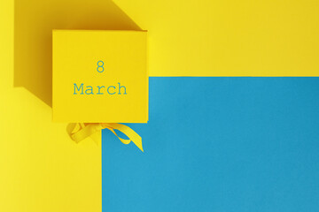 Bright yellow gift box with ribbon bow on yellow and blue  background top view copy space. Birthday present, March 8, Mothers Day, Valentines Day, Easter or spring concept.