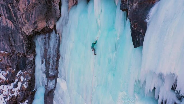 Ice Climbing on Frozen Waterfall, Aerial View. Mountaineer Man is Leading Ice. Barskoon Valley, Kyrgyzstan. Drone is Orbiting