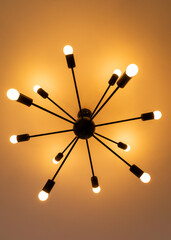 Modern minimalistic chandelier giving orange light suspended from a white ceiling