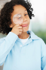 Hes a curious mind. Portrait of a cute young boy looking while holding a magnifying glass over his closed eye.