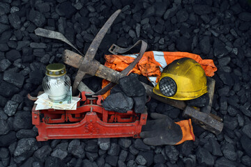 The miner belongings (helmet, gloves, pickaxe, vest, belt), graveyard candle and coal on the weight as concept after the fatal accident - obrazy, fototapety, plakaty