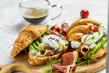 Croissant with prosciutto, poached egg, jamon, blue, cheese, avocado, microgin and cherry tomatoes. Mediterranean appetizer. Breakfast concept