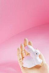 Easter Bunny in a wooden hand. White rabbit in an artificial hand on a pink background. Futuristic Easter concept. Copy space