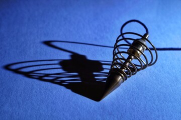 Metal dowsing pendulum and its shadow on a blue background.