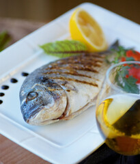 Grilled or fried fish with white wine. Decoration of vegetables and lemon. The concept of a menu for a restaurant or cafe.