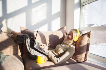 Relaxed middle-aged woman is resting at home sitting on the couch with laptop