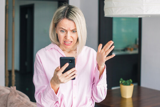 middle-aged woman holding phone, reading unpleasant news in social media