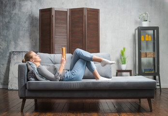 Young blonde girl is reading a book or a textbook. A beautiful woman is resting and relaxing at home.