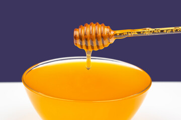 fresh fragrant honey drips from a spoon into a plate on a colored background. organic vitamin...