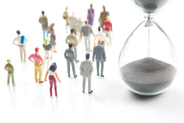 miniature people. different people are walking next to the hourglass on a white background....